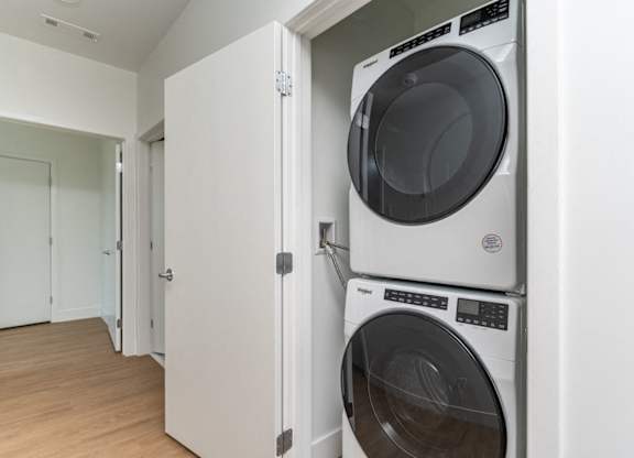 A white dryer and washer are stacked on top of each other in a small laundry room.
