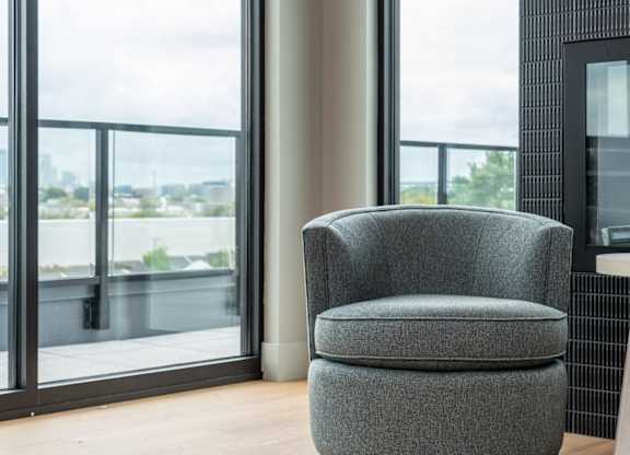 A grey chair is in front of a window with a view of a cityscape.