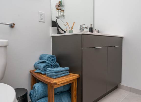 A bathroom with a grey cabinet, a white sink, and a wooden table with blue towels on it.