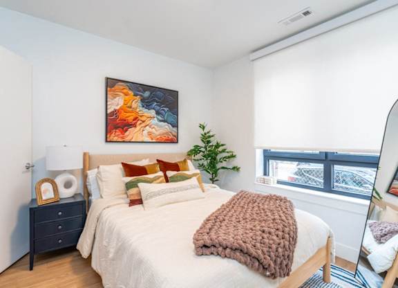 A bedroom with a bed, a nightstand, and a painting on the wall.