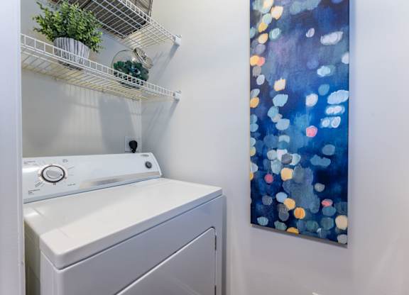 A washing machine is sitting next to a wall with a painting of blue and orange circles.