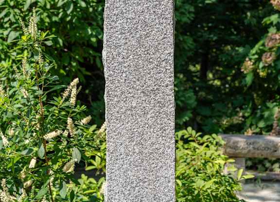 A tall, grey, rectangular memorial stone in the middle of a park.