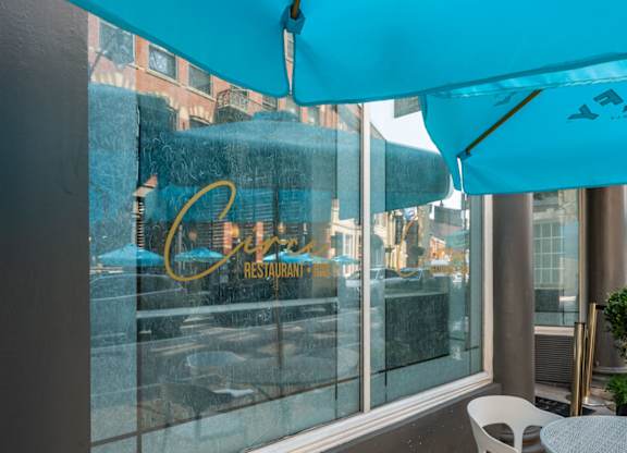 A blue umbrella is covering a table outside of a restaurant.