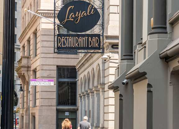 A couple walking down a sidewalk past a restaurant.