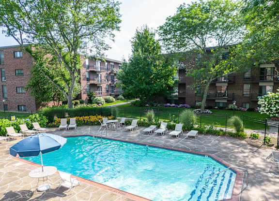 a swimming pool with chairs and an umbrella in front of an apartment building