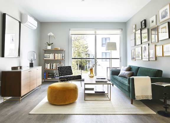 Model apartment living area with green sofa and round ottoman