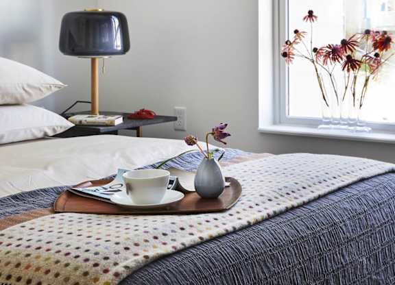 Bedroom with bed, lamp, tray with cup and vase, and window view