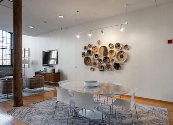 A white dining table with chairs and a wall art of plates.