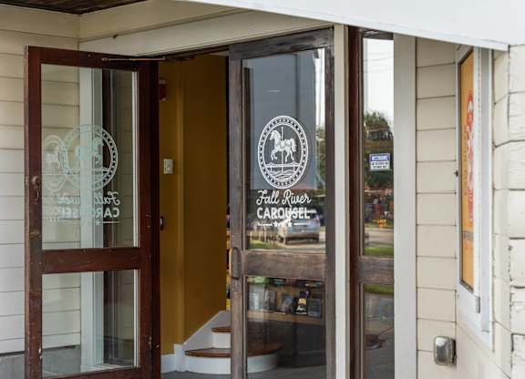 Close-up of the Fall River Carousel entrance door, featuring white horse logo etched on glass.