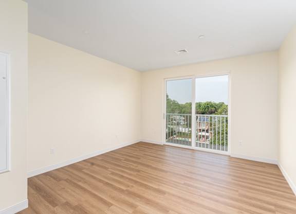 Unfurnished living area with wood-style plank flooring and tall sliding-glass doors that open to a balcony overlooking the neighborhood.