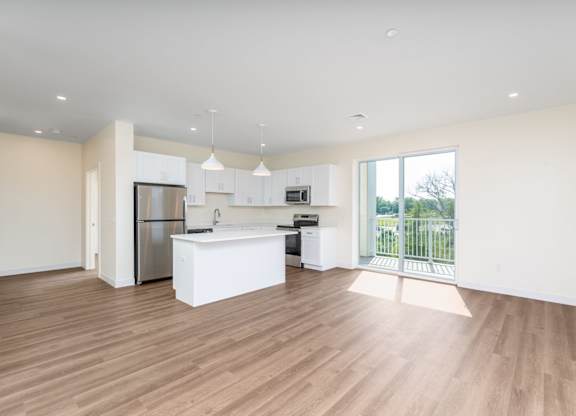 Open-concept living space combining island kitchen and lounge area, finished with wood-look flooring and a balcony door.