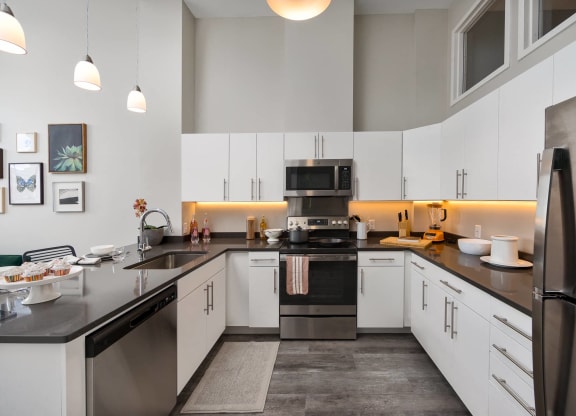 a kitchen with a large granite counter top and a sink, stainless appliances, electric range and sleek refrigerator