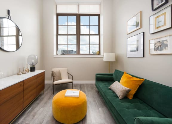 a living room with a green couch and a yellow ottoman and a window