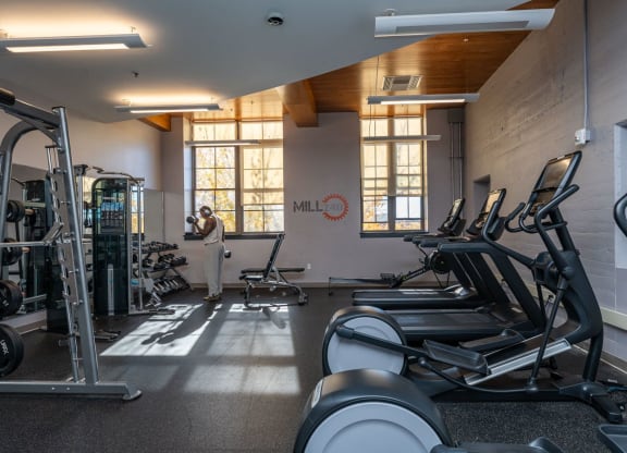 a gym with cardio equipment and a person by the window