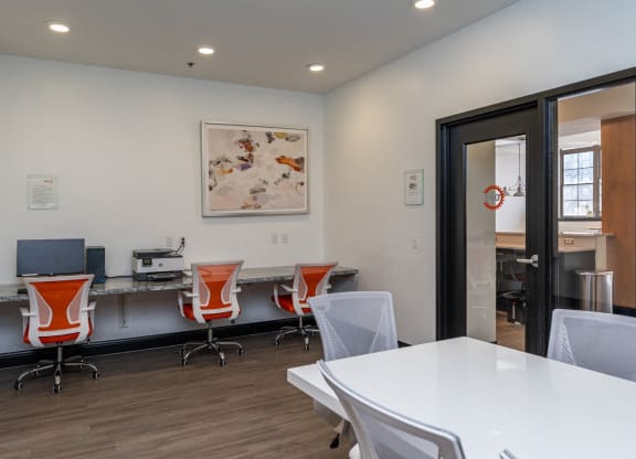 a conference room with a white table and chairs, printer, a desk with a computer