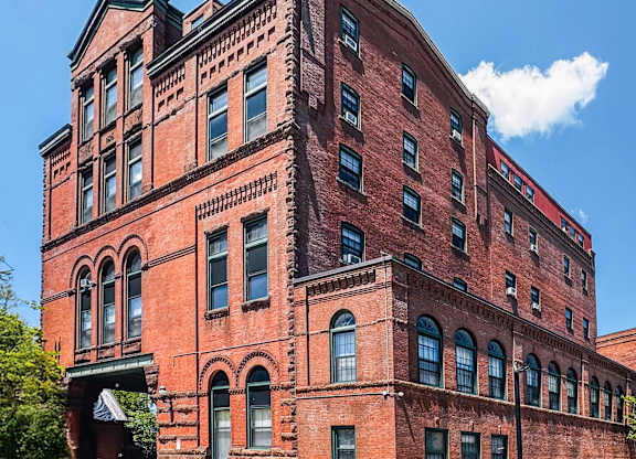 A red brick building with many windows and a balcony on the second floor at Brewery Square Apartments, New Haven