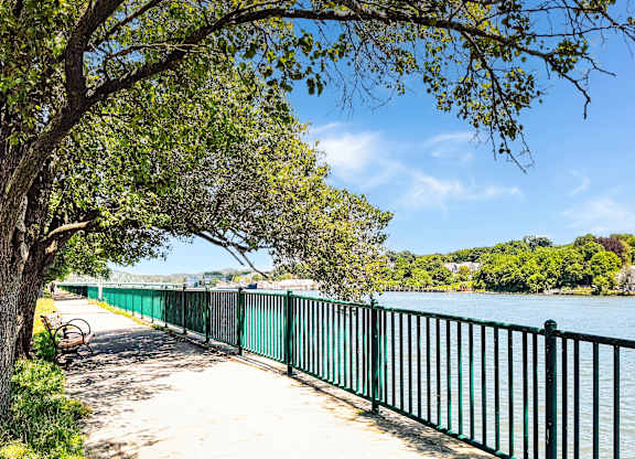 A green fence runs along a walkway next to river walk at water at Brewery Square Apartments, New Haven , CT