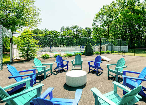 Outdoor Fire Pit with blue and green chairs are arranged in a circle at Mariner's Hill Apartments, Massachusetts.