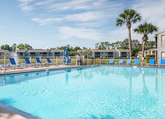 A large swimming pool with blue water and lounge chairs Fishermans Landing Apartments in Ormond Beach, FL.