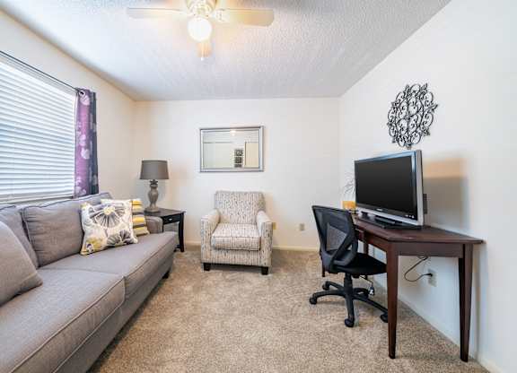 A living room with a grey couch, a chair, a table with a computer monitor and a lamp Fishermans Landing Apartments in Ormond Beach, FL.