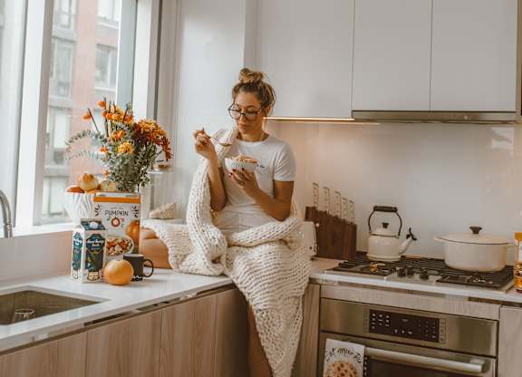 A woman is sitting on a kitchen counter with a dog beside her.
