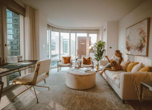 A woman is sitting on a couch in a living room with a large window and a view of the city.