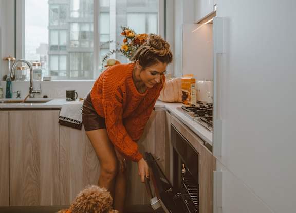 A woman in an orange top and a dog in a kitchen.