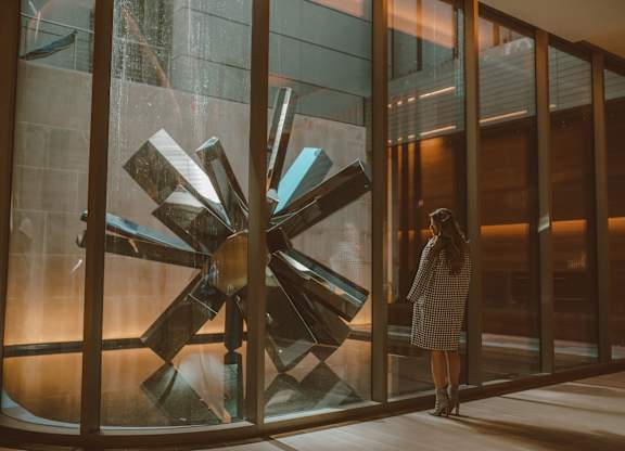A woman in a checkered dress stands in front of a glass sculpture.