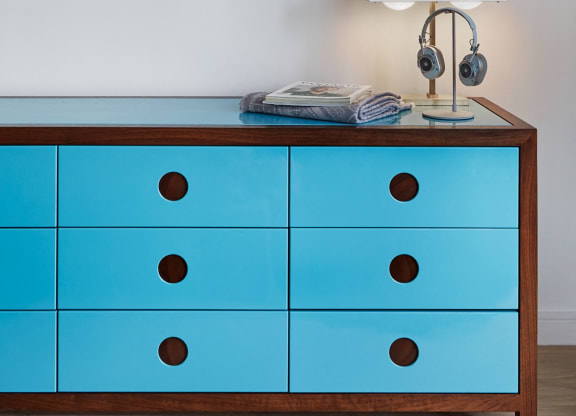 a blue dresser with a lamp and a picture on the wall above it