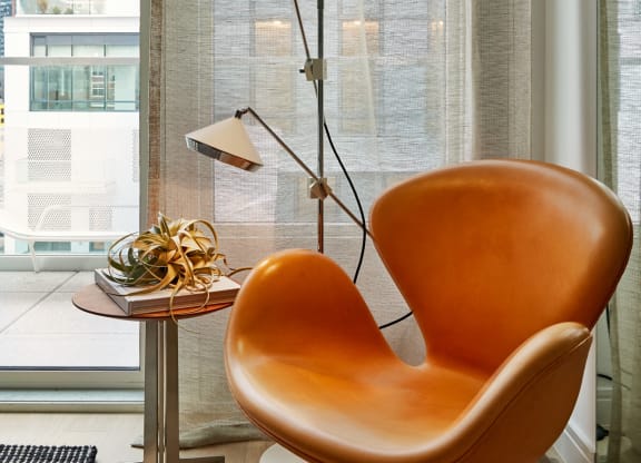 a living room with an orange chair and a table with a lamp