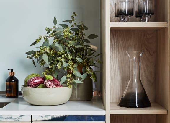 a kitchen with wooden shelves with a bowl of fruit and a vase of flowers
