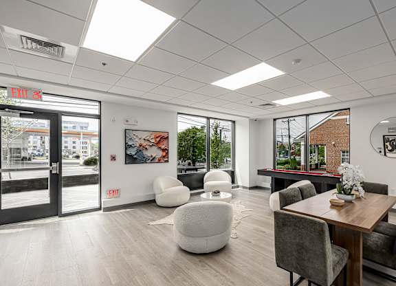 A modern office space with a wooden table and chairs, a white bean bag, and a view of the city through the windows.