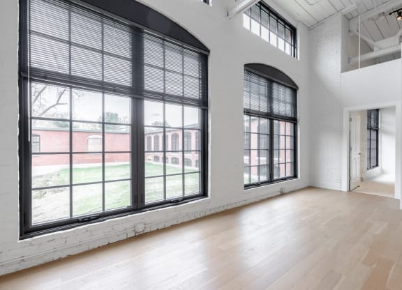 an empty living room with large windows and a wood floor