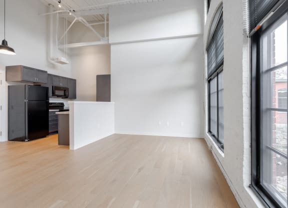an empty living room with a kitchen and a large window