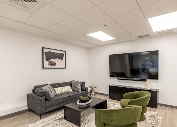A living room with a grey couch, a green chair, and a flat screen TV mounted on the wall.