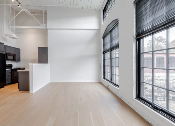 an empty living room with large windows and a kitchen