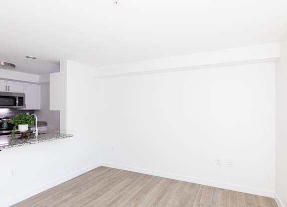 A white room with a wooden floor and a kitchen area to the left.