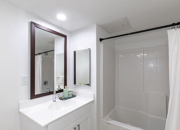 A white bathroom with a sink, mirror, and shower.