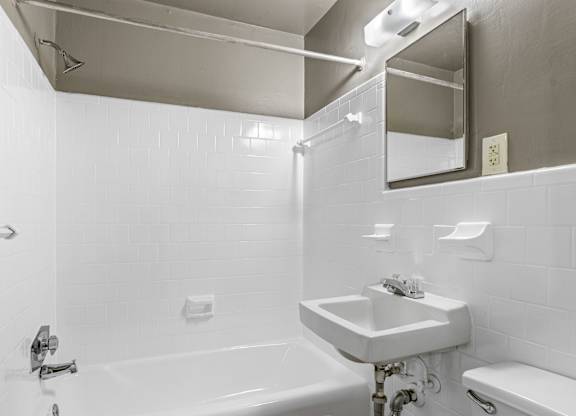 A white bathroom with a sink, mirror, and tub.