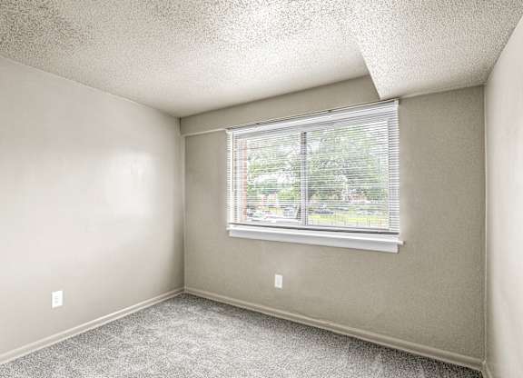 A room with a window and a carpeted floor.