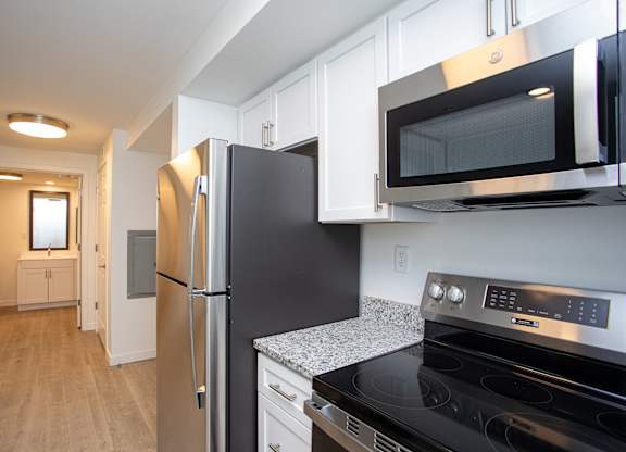 A black fridge and microwave in a kitchen with white cabinets.at The Camelot, West Hartford, 06119  