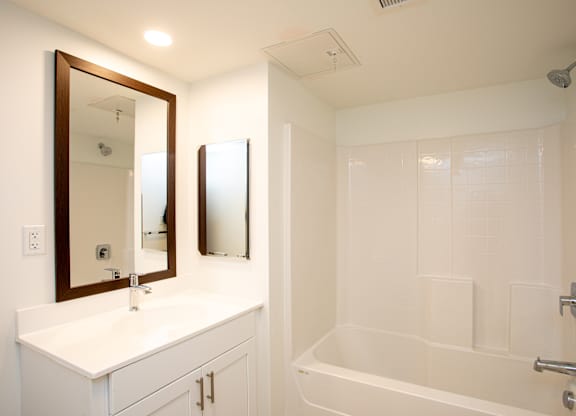 A white bathroom with a sink, mirror, and bathtub.at The Camelot, Connecticut  