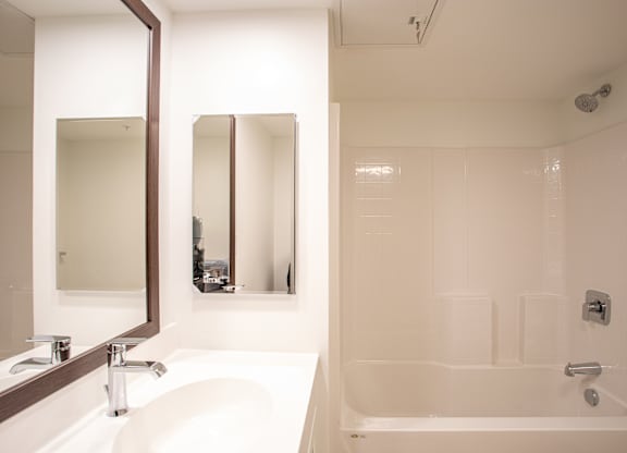 A white bathroom with a sink, mirror, and bathtub.at The Camelot, Connecticut  