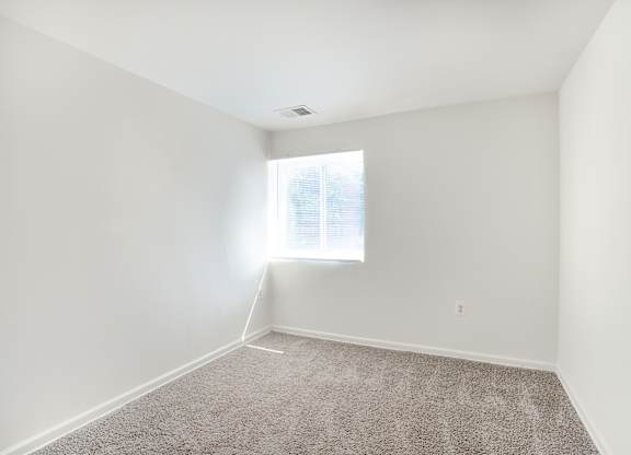 A room with a carpeted floor and a window letting in natural light.