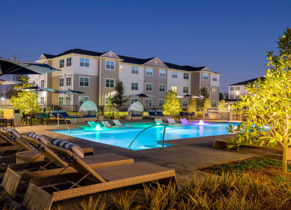a swimming pool with lounge chairs and umbrellas in front of an apartment building at 55 Fifty at Northwest Crossing, Houston, TX 77092