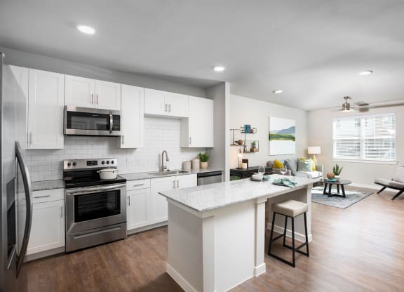 a kitchen and living room with white cabinets and stainless steel appliances at 55 Fifty at Northwest Crossing, Houston Texas