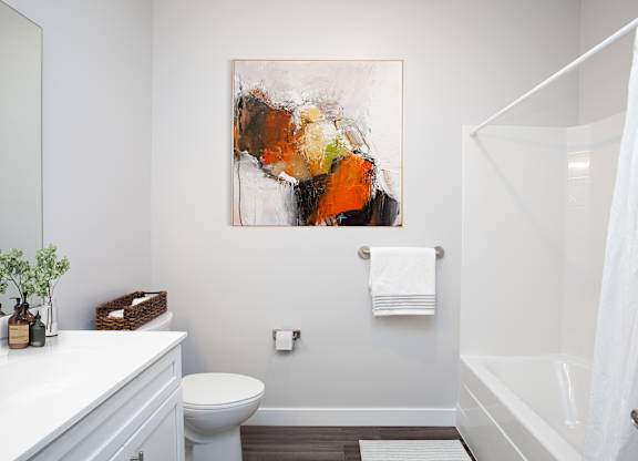 A white bathroom with a toilet, sink, and a painting on the wall.