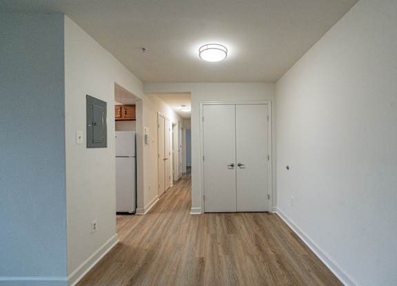 A long hallway with a refrigerator on the left and a door on the right.