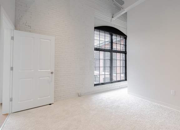 A white door is on the left side of a room with a large window and a white wall.