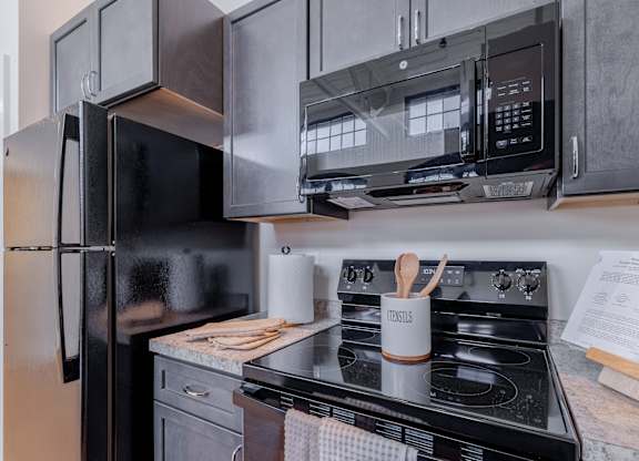 A black refrigerator and microwave are installed above a stove in a kitchen.